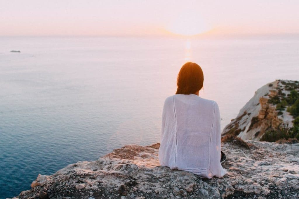 a woman sitting on top of a cliff overlooking the ocean