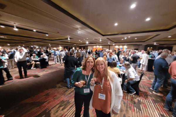 two women standing next to each other in a room full of people at a tradeshow
