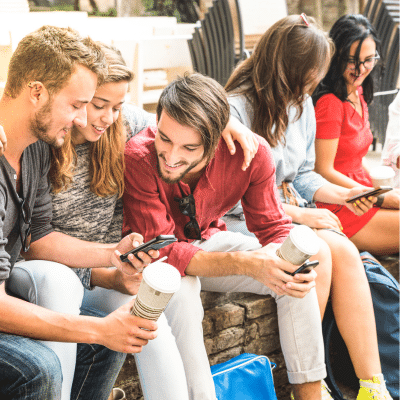 three people sitting on a stone wall looking at their cell phones